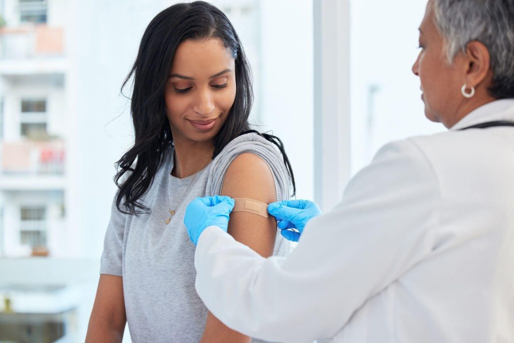 A female pharmacist putting a bandage on a woman's arm following a vaccination