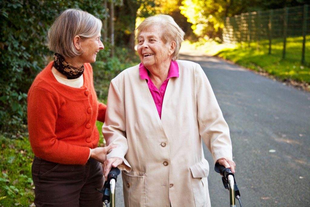 Two elderly women standing outside; one is using a walking aid