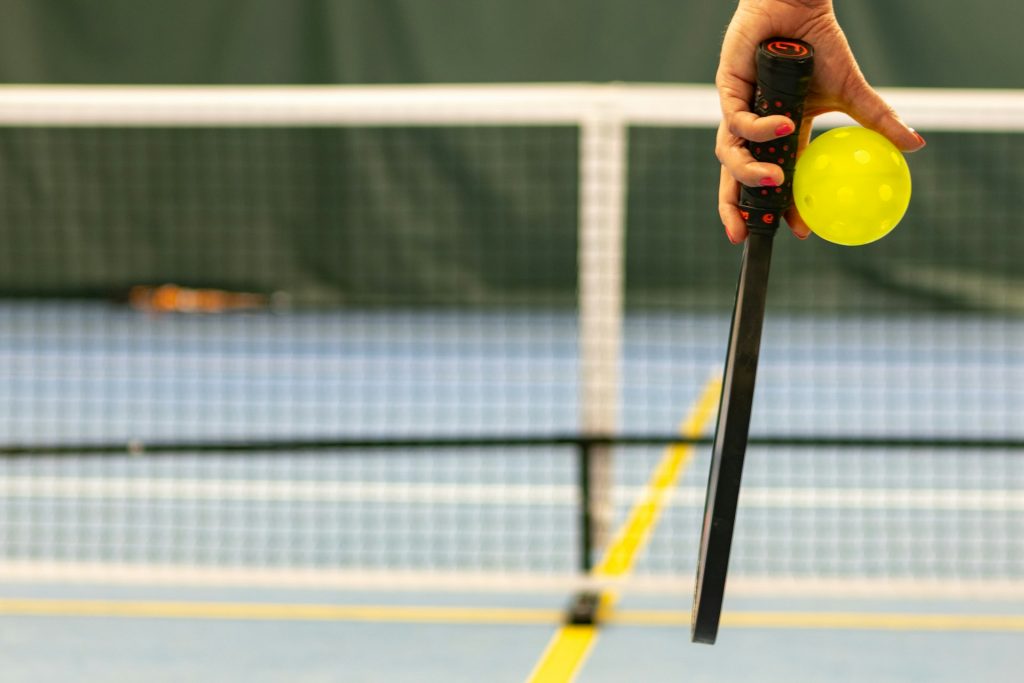 A woman's hand holding a pickleball and pickleball paddle