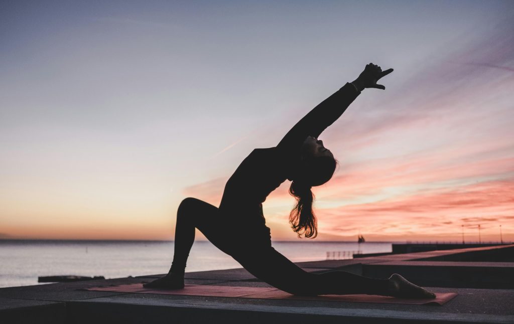 A silhouetted woman exercising by the sea at sunset