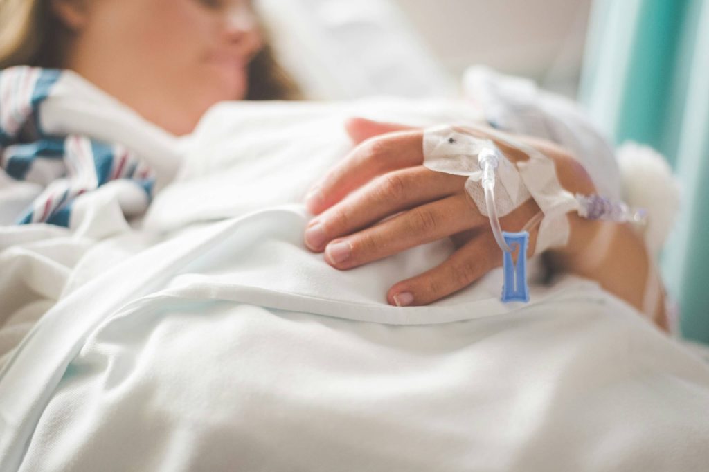 A close-up of a woman's hand with a canula as she lies in a hospital bed