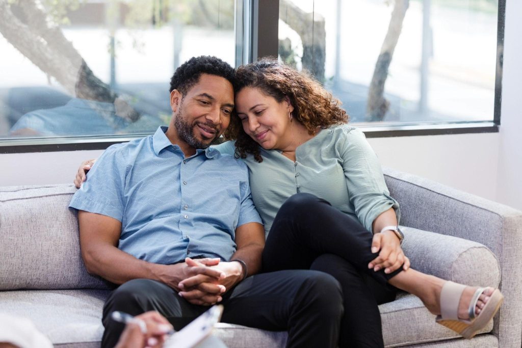 A husband and wife sitting on a sofa together during a couples therapy session